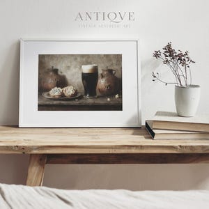May include: A framed print of a still life featuring a glass of dark beer, two ceramic jugs, and two pastries on a wooden table. The print has a vintage aesthetic and is titled "Antique Vintage Aesthetic Art".