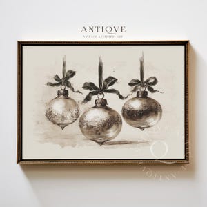 May include: A framed sepia print depicting three Christmas baubles. Each bauble is suspended by a dark ribbon and bow. The baubles have detailed patterns and are set against a neutral backdrop. The frame is gold.