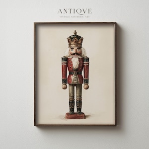 Op de afbeelding: Een ingelijste kunstdruk met een notenkraker in vintage-stijl, voorzien van een gouden kroon, een rood jasje met zwarte accenten en zwarte laarzen. De notenkraker heeft een witte baard en snor en staat op een crèmekleurige achtergrond.