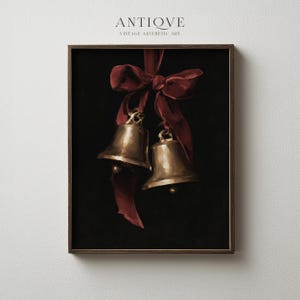 Puede incluir: Una impresión artística enmarcada que muestra dos campanas de oro metálico colgadas de una cinta roja oscura sobre un fondo negro sólido. El texto ANTIQVE VINTAGE AESTHETIC ART está impreso en letras negras pequeñas sobre el marco de madera.
