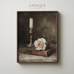 Puede incluir: Impresión artística enmarcada de época con un bodegón de una rosa blanca, una vela en un candelabro de latón y un libro. La obra de arte tiene una estética vintage con el texto "ANTIQVE" en la parte superior.