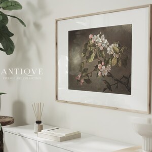 May include: A framed vintage botanical print featuring a delicate branch of white and pink blossoms with a small hummingbird perched on a twig. The print is set against a dark brown background and has a white mat.