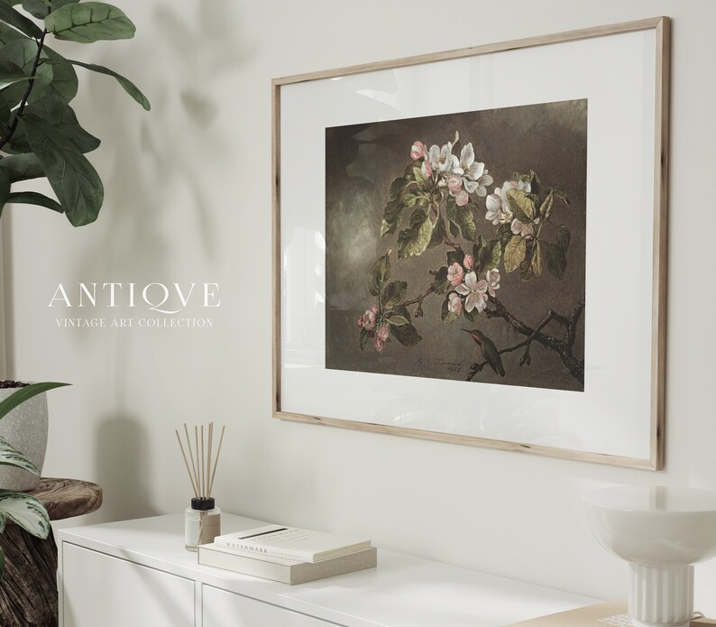 May include: A framed vintage botanical print featuring a delicate branch of white and pink blossoms with a small hummingbird perched on a twig. The print is set against a dark brown background and has a white mat.