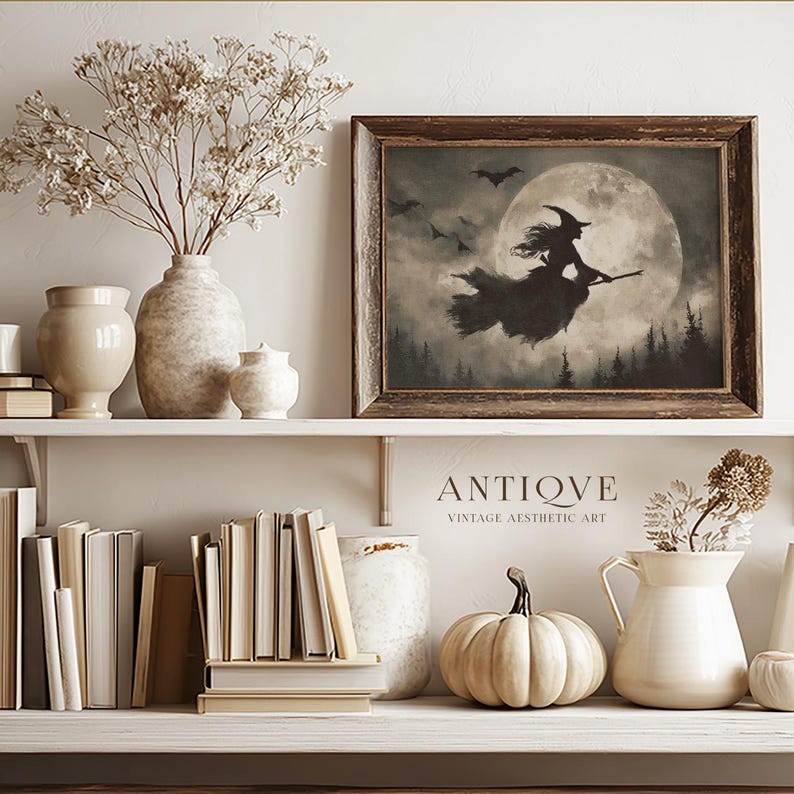 May include: A framed vintage print depicts a witch flying on a broom in front of a full moon, with bats in the sky. The print is displayed on a shelf with books, vases, and a pumpkin. The text "ANTIQUE VINTAGE AESTHETIC ART" is below the print.