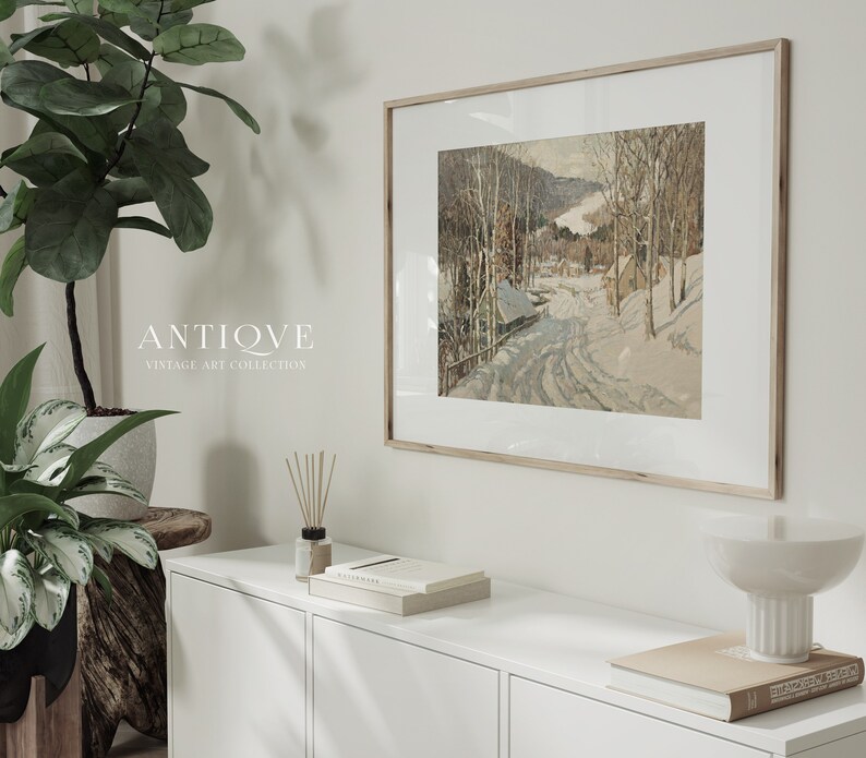 May include: A framed vintage art print of a snowy winter scene with a road leading through a forest. The print is in a light wood frame and is hanging on a white wall. The text "ANTIQVE VINTAGE ART COLLECTION" is visible below the print.