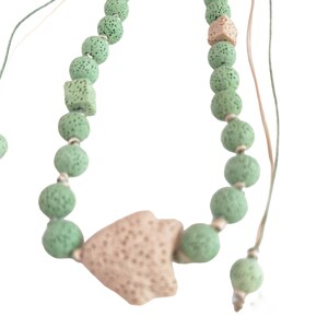 May include: A green and beige lava rock beaded necklace with a large beige lava rock pendant. The necklace is tied with two strings.
