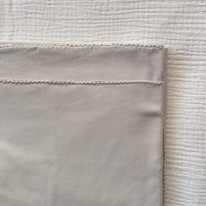 Puede incluir: Una manta beige claro con un borde cosido decorativo.