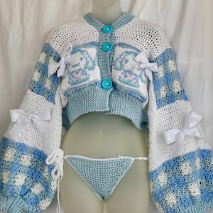 Puede incluir: Un cárdigan de crochet azul y blanco con un diseño de cinnamorroll y lazos blancos. El cárdigan tiene una longitud recortada y mangas largas. El cárdigan se combina con una braga de bikini de crochet azul a juego.