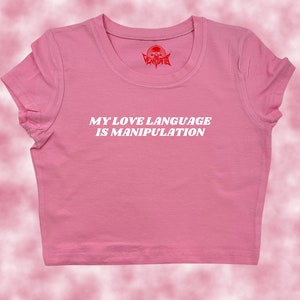 May include: Pink cropped t-shirt with the text "MY LOVE LANGUAGE IS MANIPULATION" in white letters.