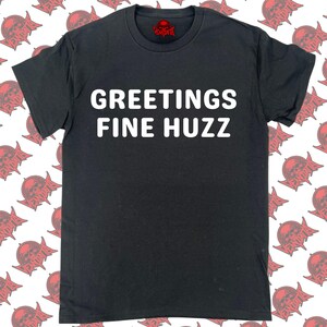 Op de afbeelding: Zwart T-shirt met witte tekst die "Greetings Fine Huzz" luidt.
