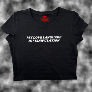 May include: Black cropped t-shirt with white text that reads "My love language is manipulation". The shirt has a red skull logo on the neck.