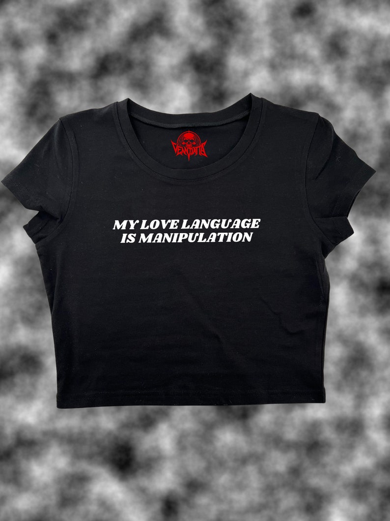 May include: Black cropped t-shirt with white text that reads "My love language is manipulation". The shirt has a red skull logo on the neck.