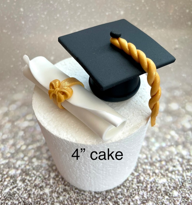 May include: A white cake with a black graduation cap and a white scroll with a gold bow on top. The cake is 4 inches in diameter and says "4" cake on the side.