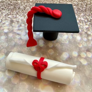 May include: A black graduation cap with a red tassel and a white scroll tied with a red ribbon. The cap and scroll are made of fondant and are perfect for a graduation cake topper.