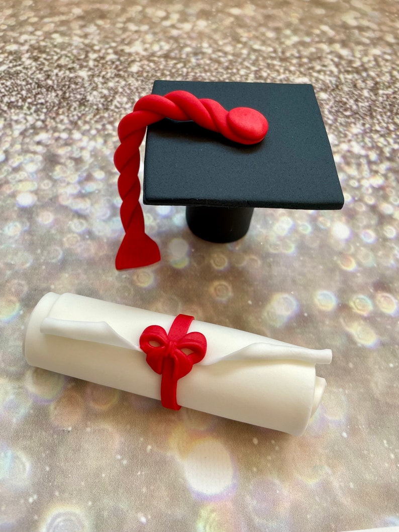 May include: A black graduation cap with a red tassel and a white scroll tied with a red ribbon. The cap and scroll are made of fondant and are perfect for a graduation cake topper.