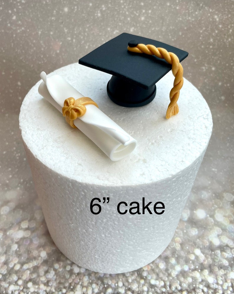 May include: A 6 inch cake decorated with a black graduation cap with a gold tassel and a white scroll with a gold ribbon.