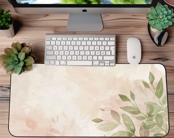 Può includere: Un tappetino da scrivania in acquerello rosa chiaro e verde con un design a foglia. Il tappetino è su una scrivania di legno con un computer, una tastiera e un mouse.