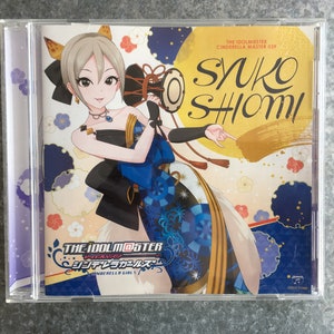 May include: A CD case featuring a colorful illustration of a woman in a blue and gold kimono holding a drum. The text "THE IDOLM@STER CINDERELLA MASTER 039 SYUKO SHIOmi" is printed on the case.