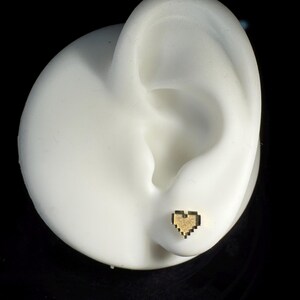 May include: A gold pixelated heart stud earring on a white ear model.