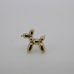 Puede incluir: Una figura de perro globo de color dorado. El perro est&aacute; de pie, con su cuerpo y extremidades formados por formas redondeadas y conectadas, imitando un animal de globo. La figura tiene una superficie brillante y reflectante.