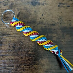May include: A yellow, white, blue, and red braided keychain with a silver key ring.