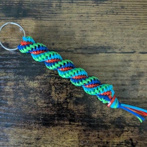 May include: A colorful, braided key chain with a silver key ring. The braid is made of green, blue, and red string.