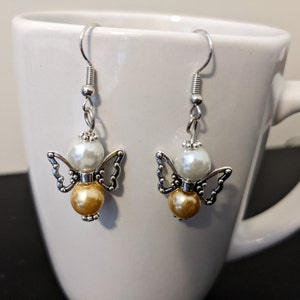 May include: A pair of silver angel-shaped earrings with white and gold pearl beads.