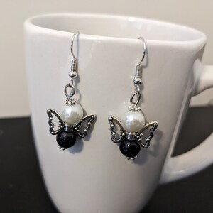 May include: Silver dangle earrings with a white pearl and black bead, shaped like a butterfly.
