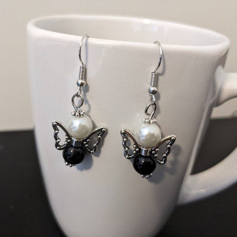 May include: Silver dangle earrings with a white pearl and black bead, shaped like a butterfly.