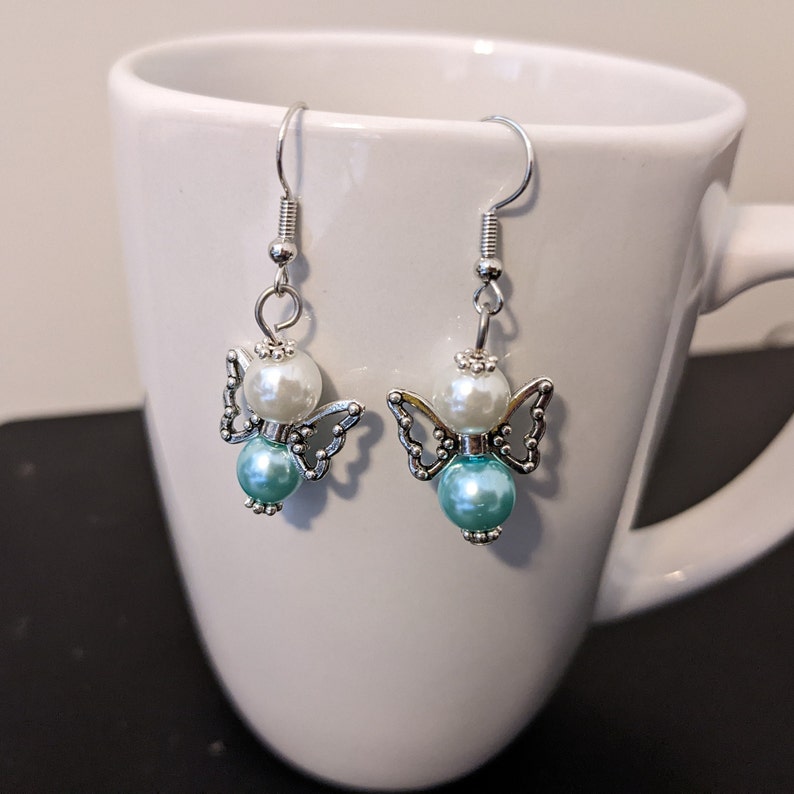 May include: A pair of silver angel wing earrings with white and turquoise beads.