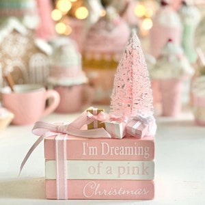 Puede incluir: Una pila de tres bloques de madera pintados de rosa con letras blancas. El bloque superior dice "I'm Dreaming of a pink Christmas". Los bloques est&aacute;n decorados con una cinta rosa y un peque&ntilde;o &aacute;rbol de Navidad rosa con purpurina blanca. Tambi&eacute;n hay peque&ntilde;os regalos envueltos en la parte superior de los bloques.