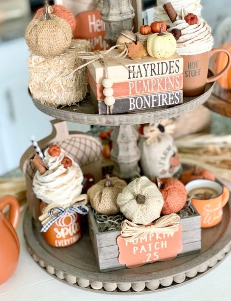 May include: A tiered tray decorated with fall-themed items, including pumpkins, a mug with the text "Hot Stuff", a jar with the text "Spice Everything", and a wooden box with the text "Pumpkin Patch .25".