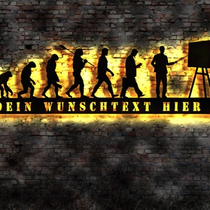 Puede incluir: Una silueta negra de metal de la evolución del hombre, que termina con un hombre sosteniendo un puntero frente a una pizarra en blanco. La silueta está iluminada con luz amarilla y el texto "DEIN WUNSCHTEXT HIER!" está debajo de la silueta.