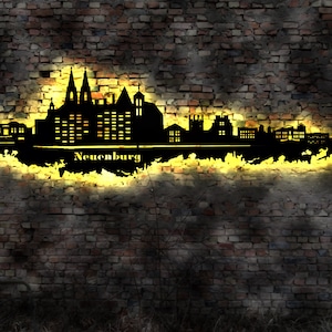 May include: Black silhouette of a city skyline with the word "Neuenburg" below it. The silhouette is lit up with a yellow glow against a brick wall background.