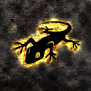 May include: A black silhouette of a gecko lizard on a brick wall with a yellow glow around it.