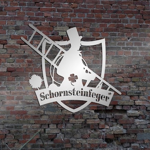 Op de afbeelding: Een metalen silhouet van een schoorsteenveger met een ladder op een bakstenen muur. Het silhouet heeft de vorm van een schild en bevat de tekst "Schornsteinfeger".