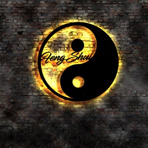 Può includere: Un simbolo yin yang in bianco e nero con un bagliore dorato, su uno sfondo di muro di mattoni. Le parole "Feng Shui" sono scritte in corsivo all'interno del simbolo.