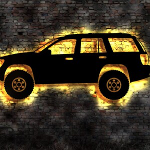 Puede incluir: Silueta de un SUV negro contra una pared de ladrillo con un brillo amarillo alrededor del vehículo.