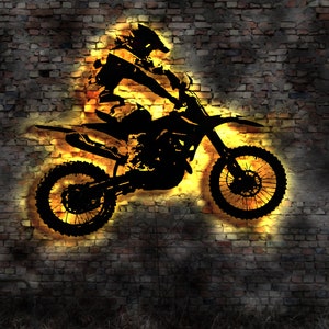 May include: Silhouette of a motocross rider on a dirt bike, jumping over a brick wall. The image is in black and white with a yellow glow around the rider and bike.