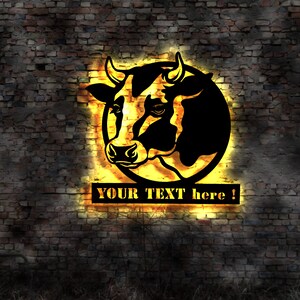 May include: Black metal cow head silhouette with a yellow glowing outline, set against a brick wall. The text "YOUR TEXT here !" is displayed in a rectangular panel below the cow's head.