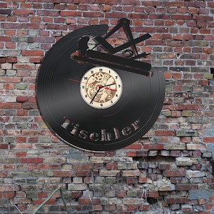 Puede incluir: Un reloj de vinilo negro con una esfera de madera y engranajes. La esfera del reloj tiene números romanos y las palabras "Tischler" están escritas en el disco.