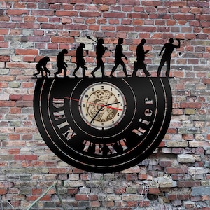 May include: A black vinyl record clock with a clock face featuring a gear design. The clock is mounted on a brick wall and features a silhouette of the evolution of man, with the last figure holding a smartphone. The clock face reads "DEIN TEXT HIER".