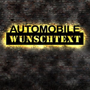 Könnte beinhalten: Ein schwarzes Schild mit weißen Buchstaben an einer Backsteinmauer. Das Schild lautet "AUTOMOBILE WUNSCHTEXT".