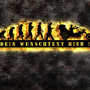 May include: Black metal wall art depicting the evolution of man, culminating in a person riding a three-wheeled motorcycle. The art piece is illuminated with yellow light and includes the text "DEIN WUNSCHTEXT HIER!"