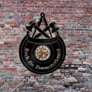 Puede incluir: Reloj de pared de metal negro con un diseño de hoja de sierra y el texto "Hoch die Zimmerekunst". La esfera del reloj presenta un reloj de madera con engranajes y una aguja de minutos roja.