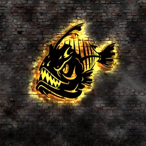 Puede incluir: Una silueta negra de un pez con dientes afilados y un contorno amarillo brillante, sobre un fondo de pared de ladrillo oscuro.