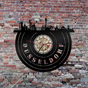 Könnte beinhalten: Schwarze Schallplattenuhr mit einer Skyline-Silhouette von Düsseldorf, Deutschland. Das Zifferblatt der Uhr hat ein Zahnrad-Design und römische Ziffern für die Stunden.