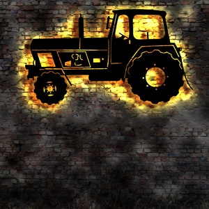 Op de afbeelding: Een zwart silhouet van een tractor met een gele gloed erachter, op een achtergrond van een bakstenen muur.