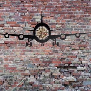 Könnte beinhalten: Eine schwarze Flugzeuguhr aus Metall, die an einer Backsteinwand montiert ist. Das Zifferblatt der Uhr hat ein Zahnrad-Design.