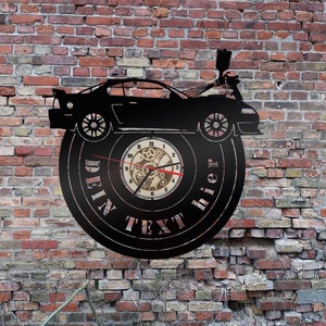 Könnte beinhalten: Schwarze Wanduhr mit einem Auto-Silhouette-Design, montiert auf einer Schallplatte. Das Zifferblatt zeigt sichtbare Zahnräder und Zeiger, mit dem Text "DEIN TEXT hier" am Rand. Die Uhr ist vor einer verwitterten Backsteinmauer angebracht.